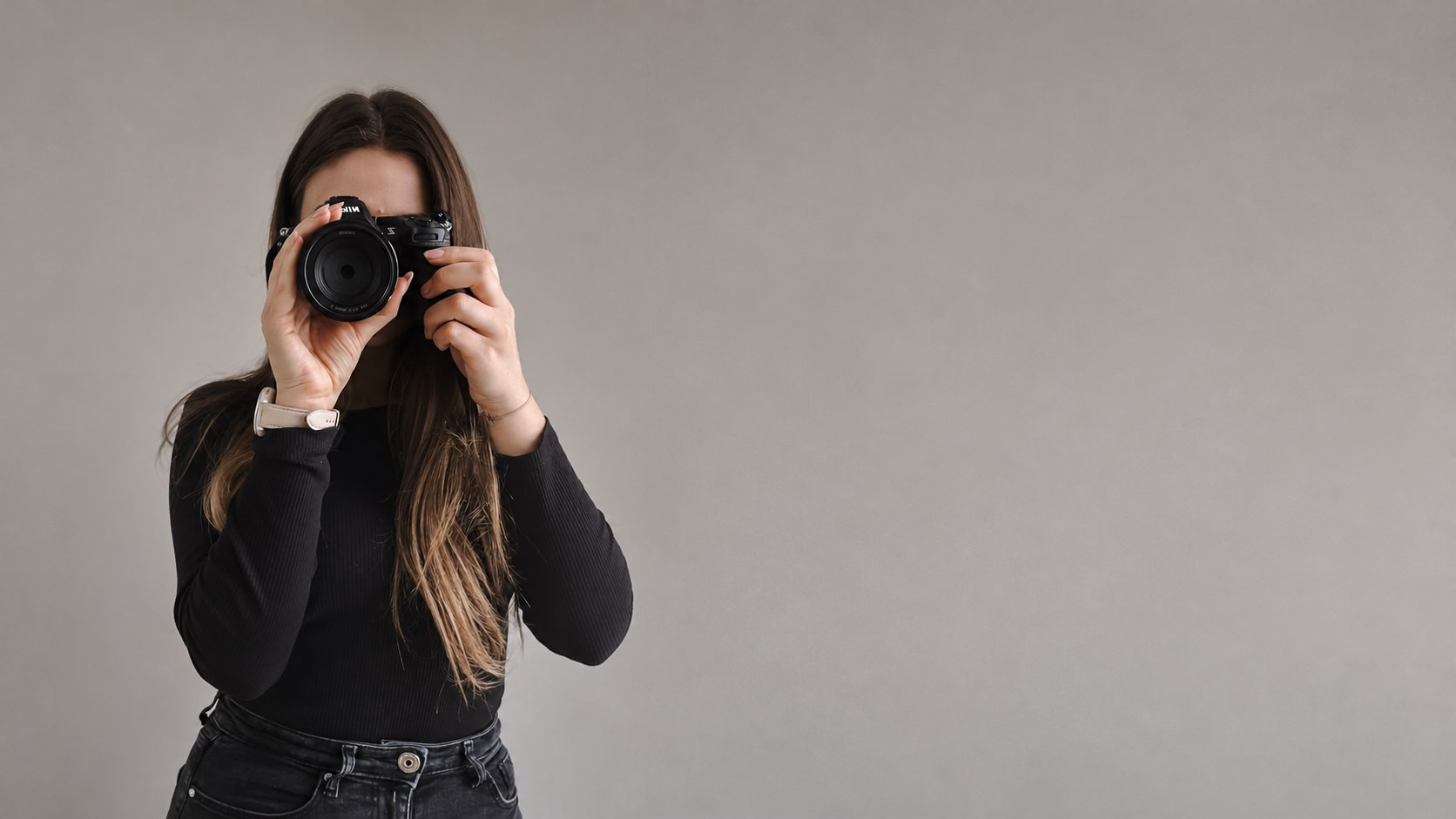 Patrycja fotografuje aparatem na tle jasnej ściany